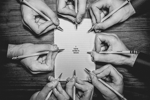 black and white photo of many hands writing on one piece of paper